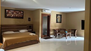 A hotel room with a bed, a desk, chairs, and artwork on the walls. - Gora Beach Inn (Kuta)