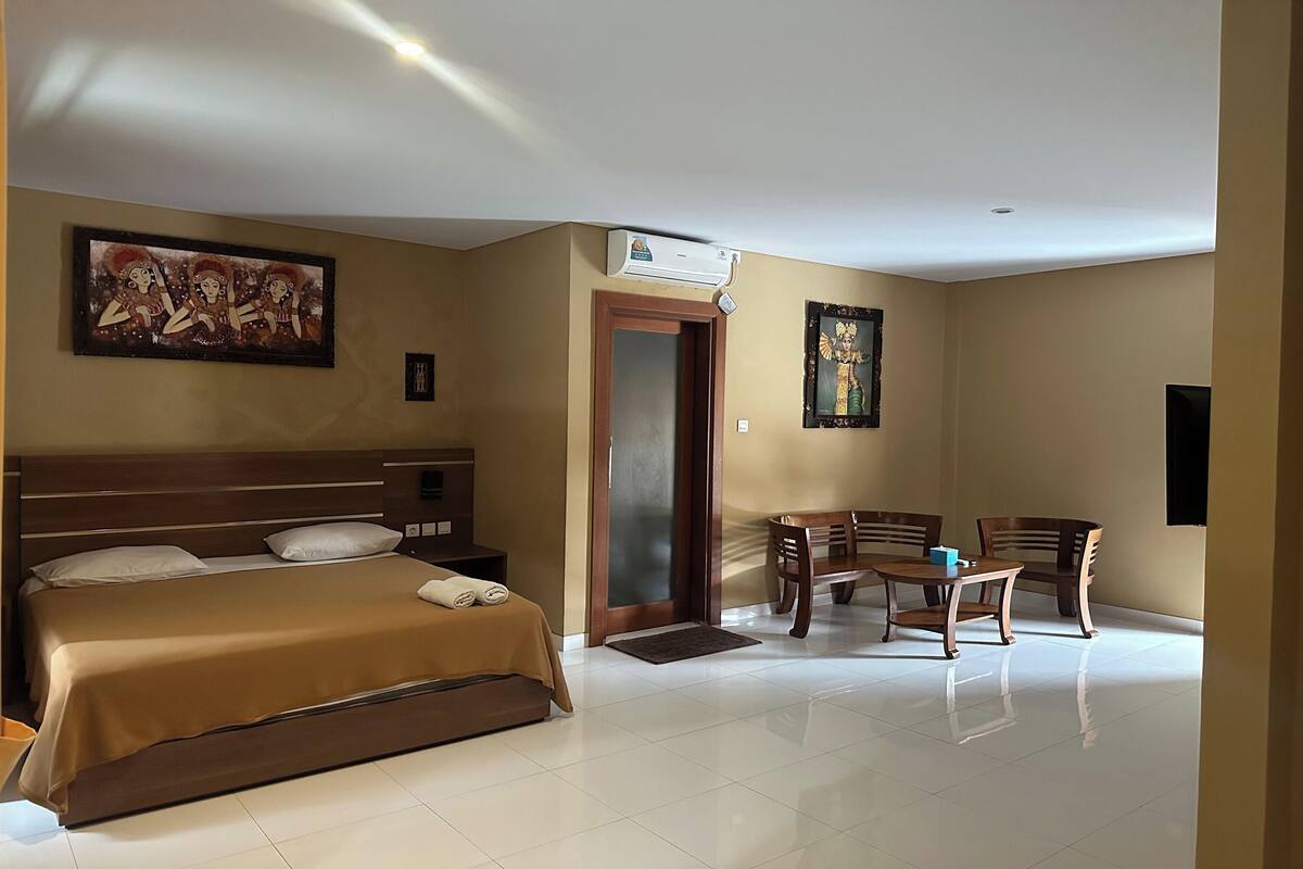 A hotel room with a bed, a desk, chairs, and artwork on the walls.