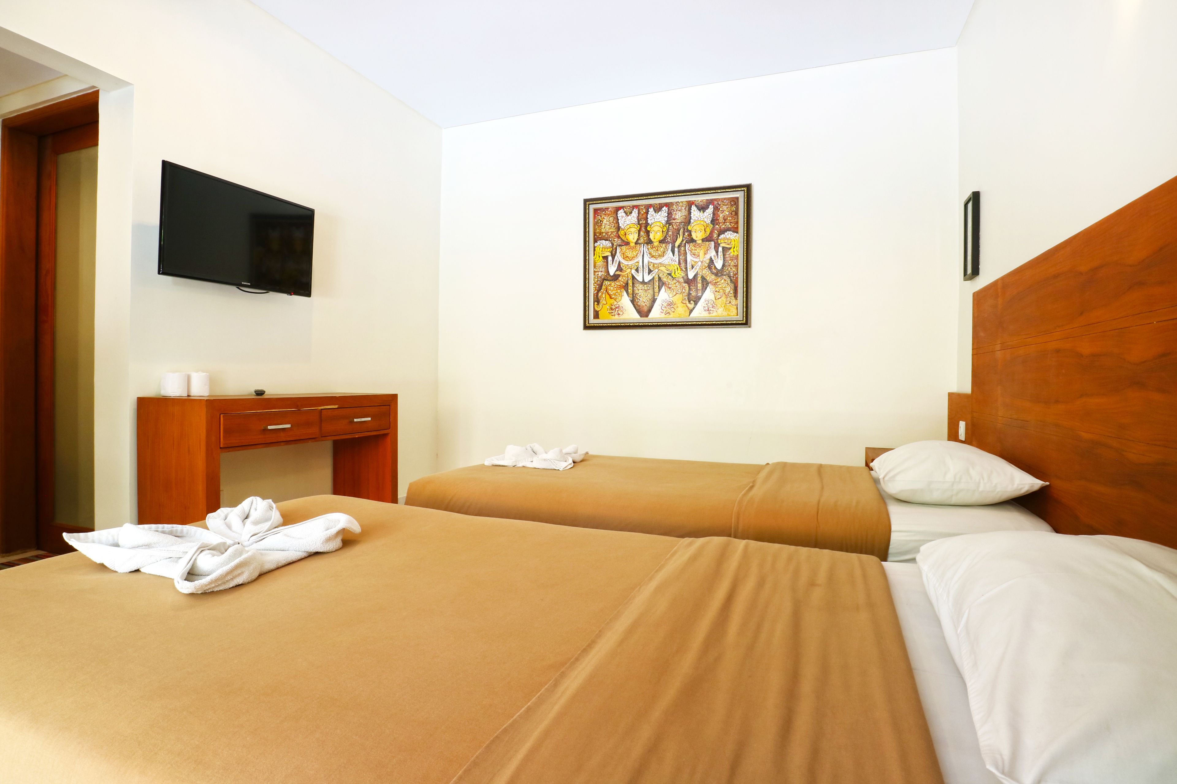 A hotel room with two beds, a TV mounted on the wall, a desk with a chair, and a painting on the wall.