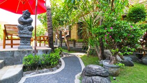 A garden pathway with a statue, a red umbrella, and a bench. - Gora Beach Inn (Kuta)