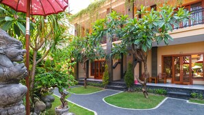 A courtyard with a stone lion statue, potted plants, and a red umbrella. - Gora Beach Inn (Kuta)