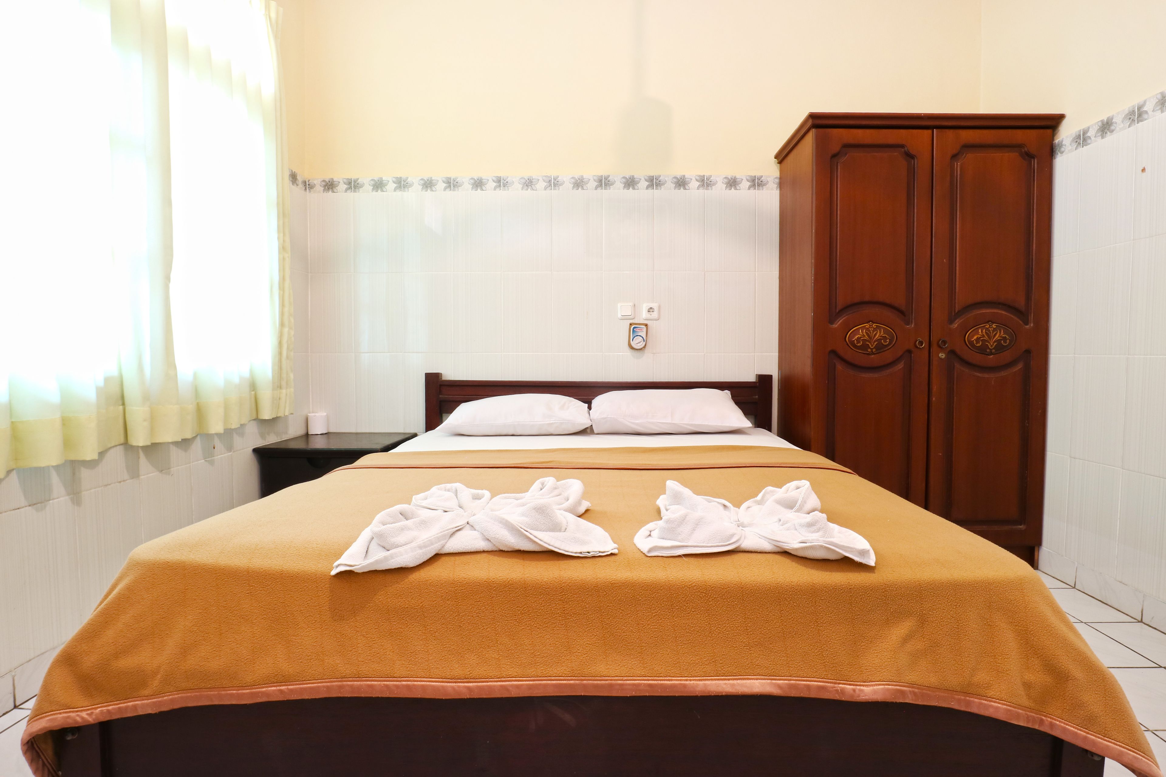 A hotel room with a bed, a wooden wardrobe, and a window with curtains.