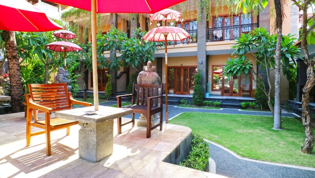 An outdoor patio area with red umbrellas, wooden chairs, and a stone table. - Gora Beach Inn (Kuta)