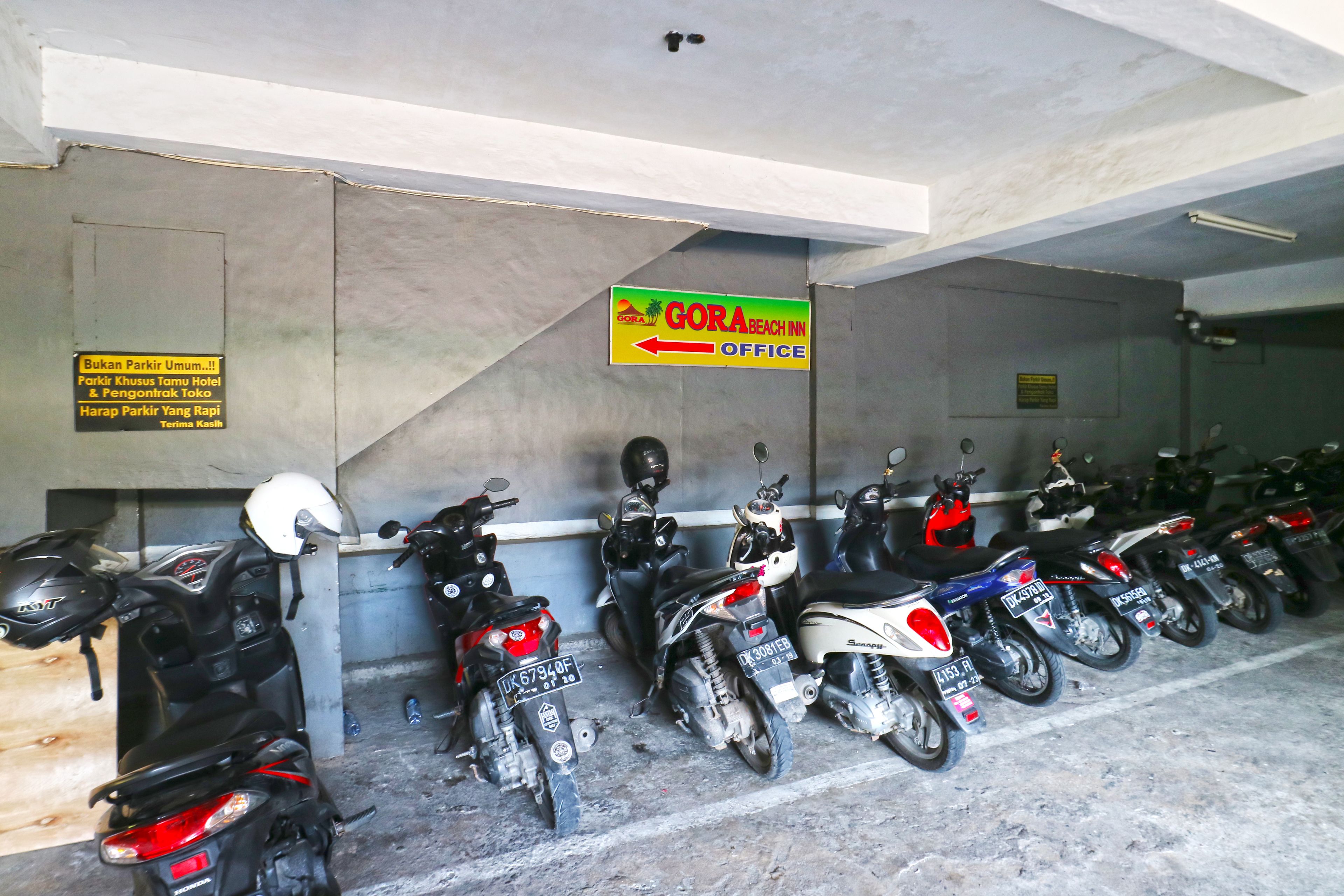 A row of motorcycles parked in a covered area with a sign indicating the GORA BEACH INN Office.
