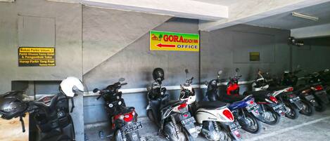 A row of motorcycles parked in a covered area with a sign indicating the GORA BEACH INN Office.