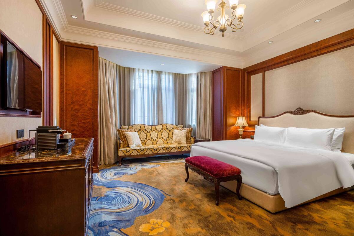 A hotel room with a bed, a desk, a sofa, and a chandelier.