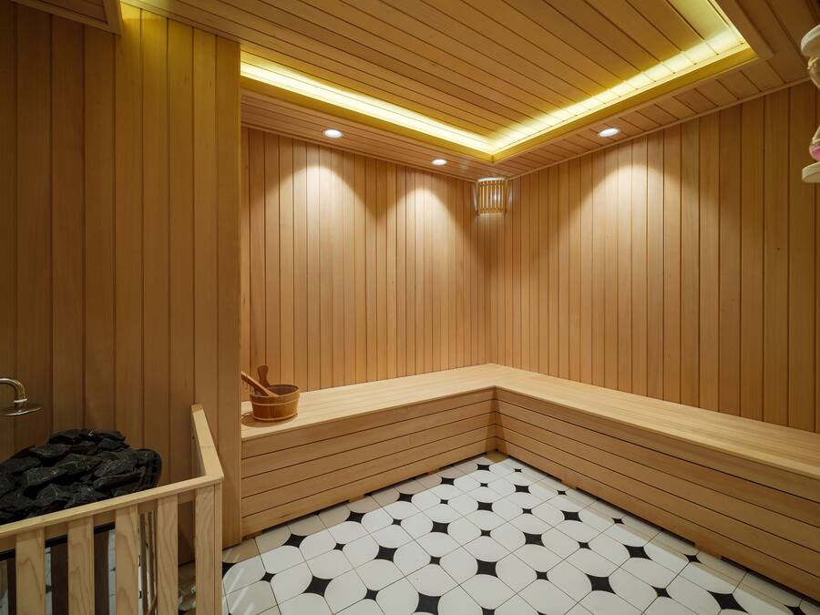 Una sauna amb parets i bancs de fusta, un terra d'rajola i un cubell de fusta.