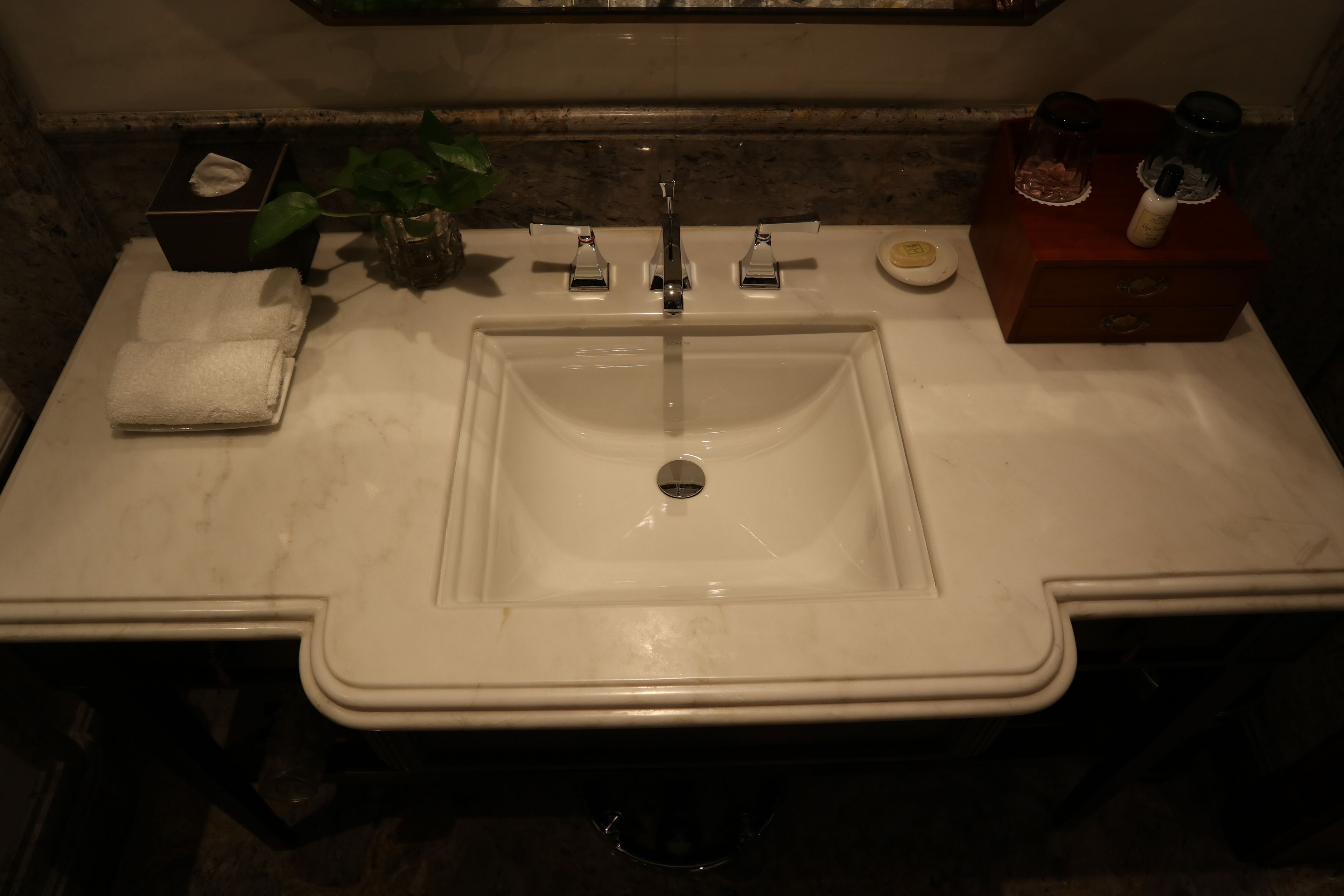 Een badkamer met een wit wastafel, een spiegel, een handdoek, een plant en toiletartikelen op het aanrecht.