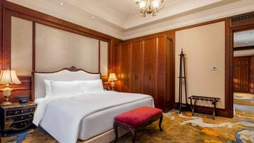 A hotel room with a large bed, wooden paneling, a standing lamp, a bench, and a carpeted floor.
