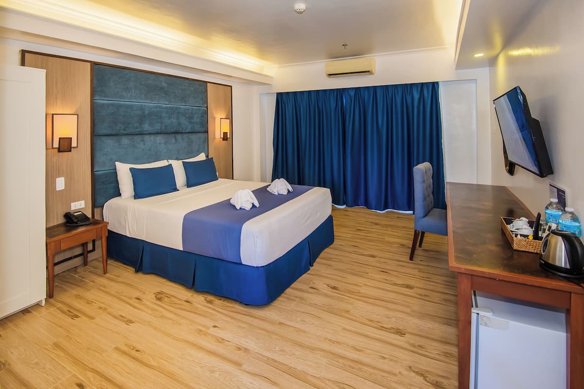 Habitación de hotel con cama, mesita de noche, escritorio, silla y televisor de pantalla plana.
