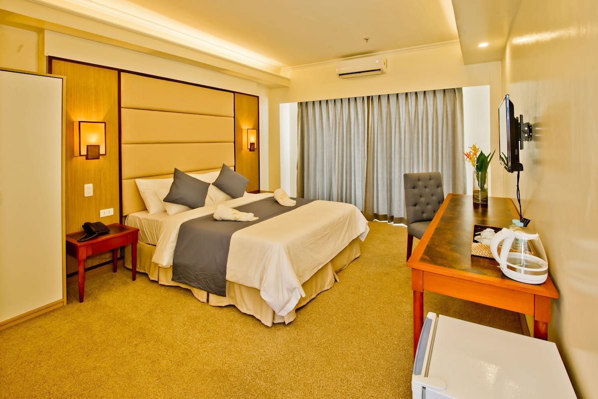 Habitación de hotel con cama, mesita de noche, silla, escritorio y televisor.