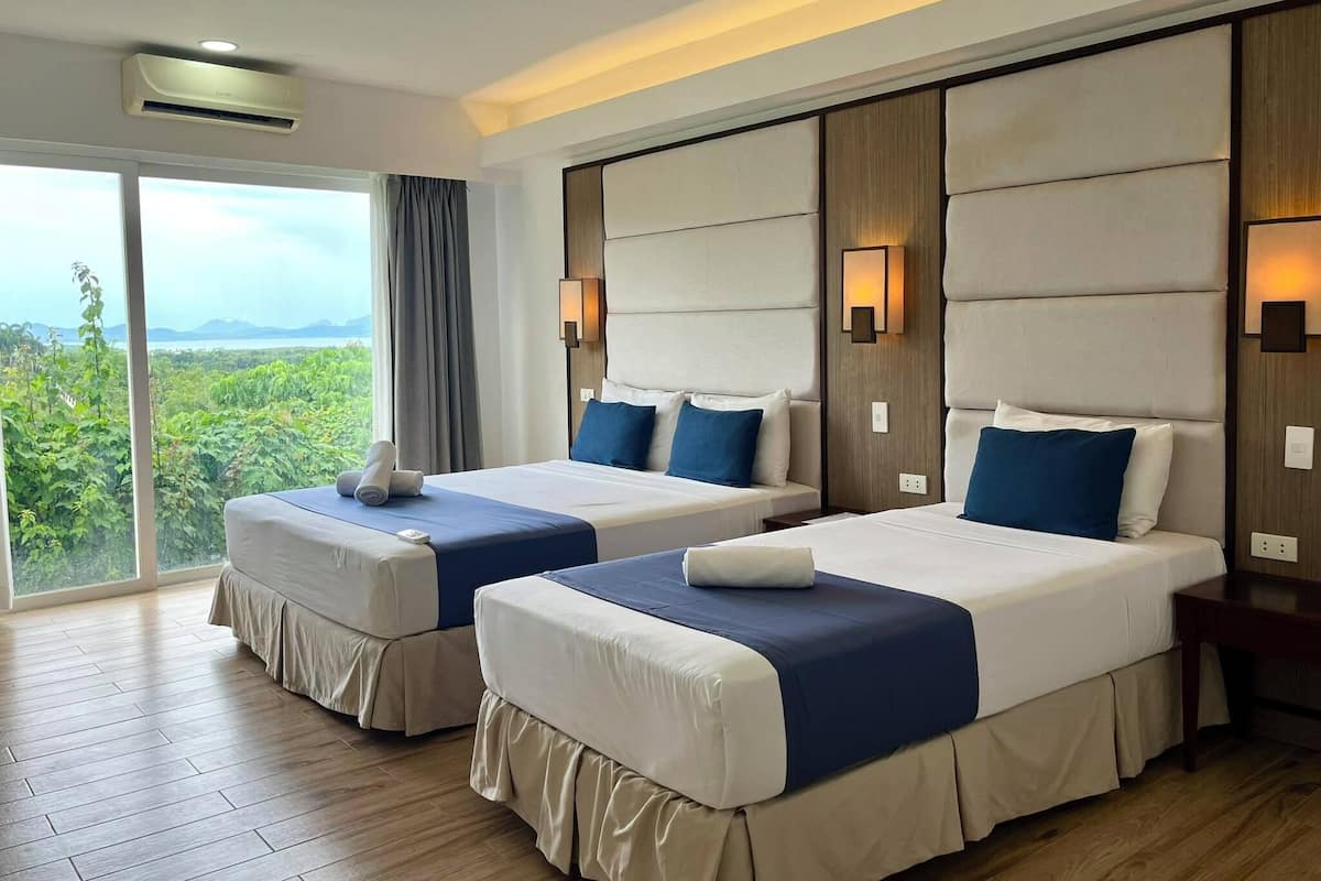 Habitación de hotel con dos camas, un ventanal con vistas a zonas verdes y aire acondicionado en el techo.