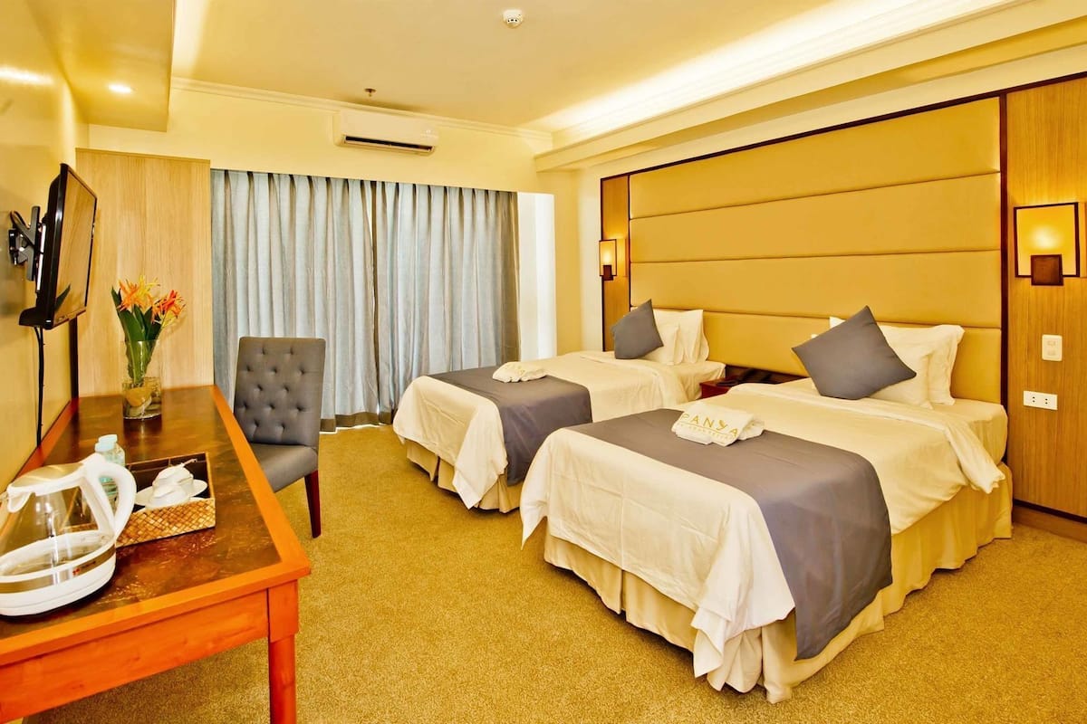 Habitación de hotel con dos camas, un escritorio, una silla, un televisor y una ventana con cortinas.