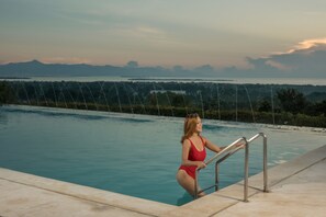 A woman in a red swimsuit at the edge of a pool with a view of mountains and a body of water in the background. - Panja Resort Palawan (Puerto Princesa)