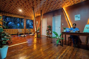 Una habitación con piso de madera, un mostrador de recepción y una puerta. Hay plantas en macetas y un amplio ventanal con vistas.