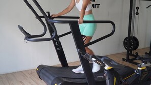 A person using a stationary bike in a gym with a weight rack in the background. - Panja Resort Palawan (Puerto Princesa)