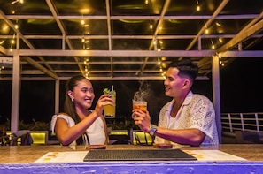 Two people toasting with drinks at a bar with a glass ceiling and string lights. - Panja Resort Palawan (Puerto Princesa)