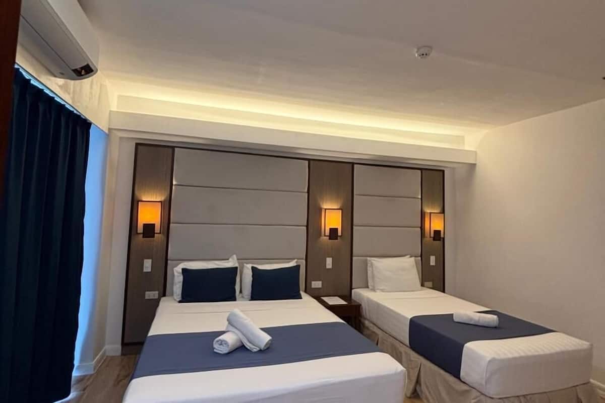 Habitación de hotel con dos camas, un cabecero grande, luces fijadas a la pared y suelo de madera.