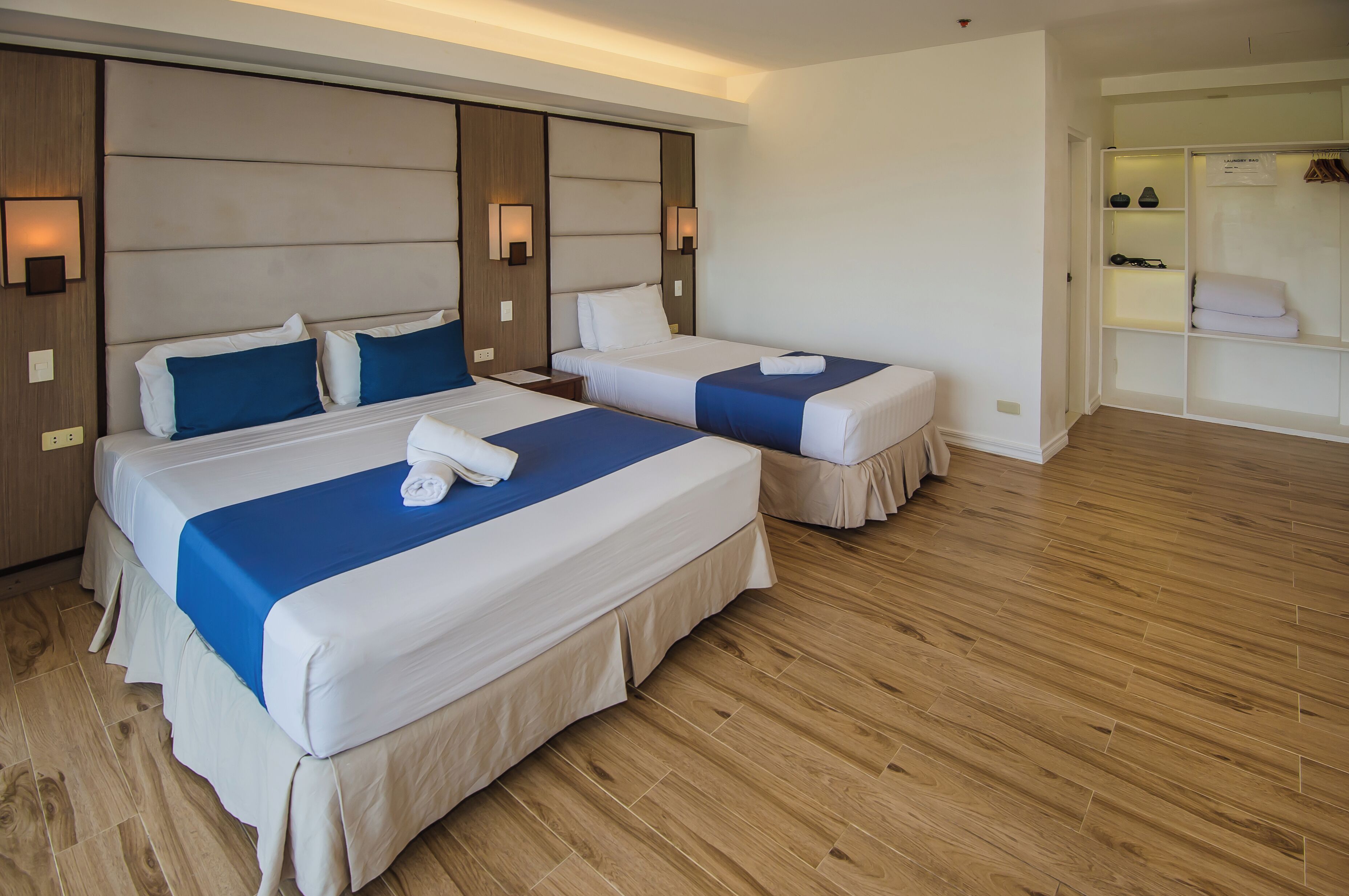 Une chambre d’hôtel avec deux lits, un plancher en bois et un placard intégré avec des étagères.