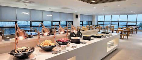 Disposição moderna de buffet com diversos alimentos e área de estar com mesas e cadeiras.
