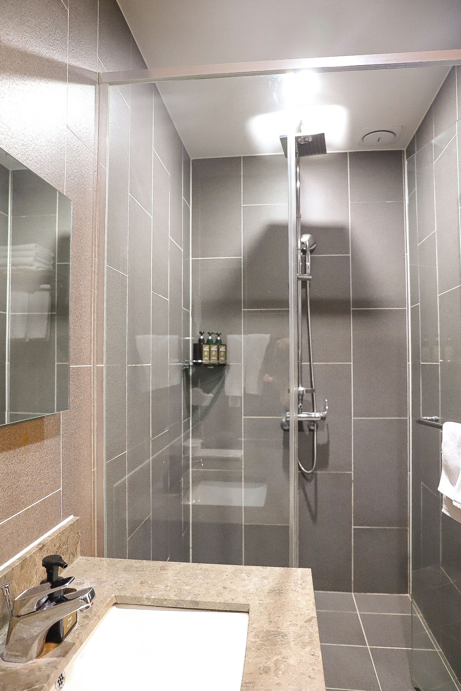A modern bathroom with a glass shower enclosure, a sink with a mirror, and a towel rack.
