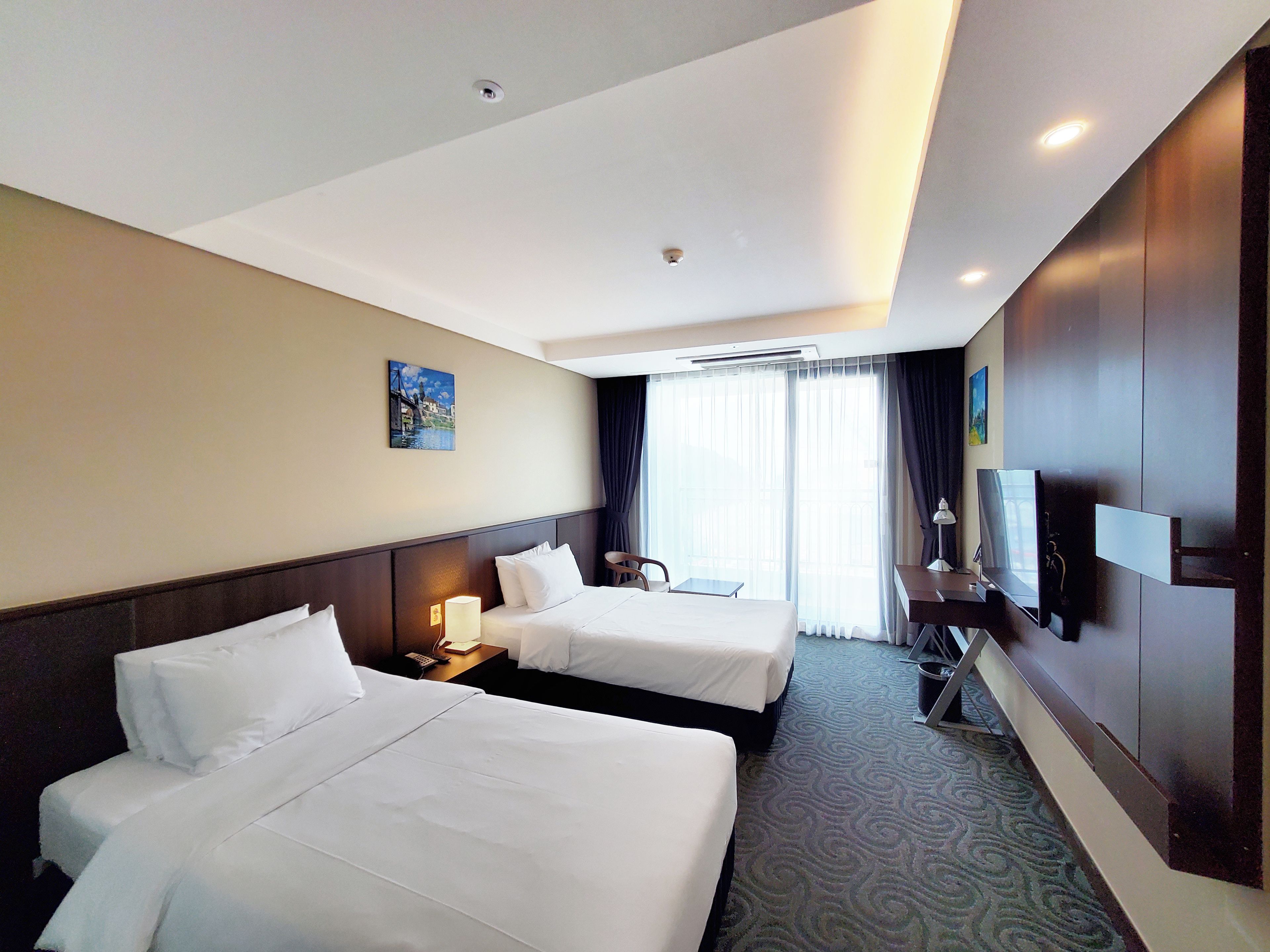 A hotel room with two beds, a desk, a chair, a TV, and a painting on the wall.