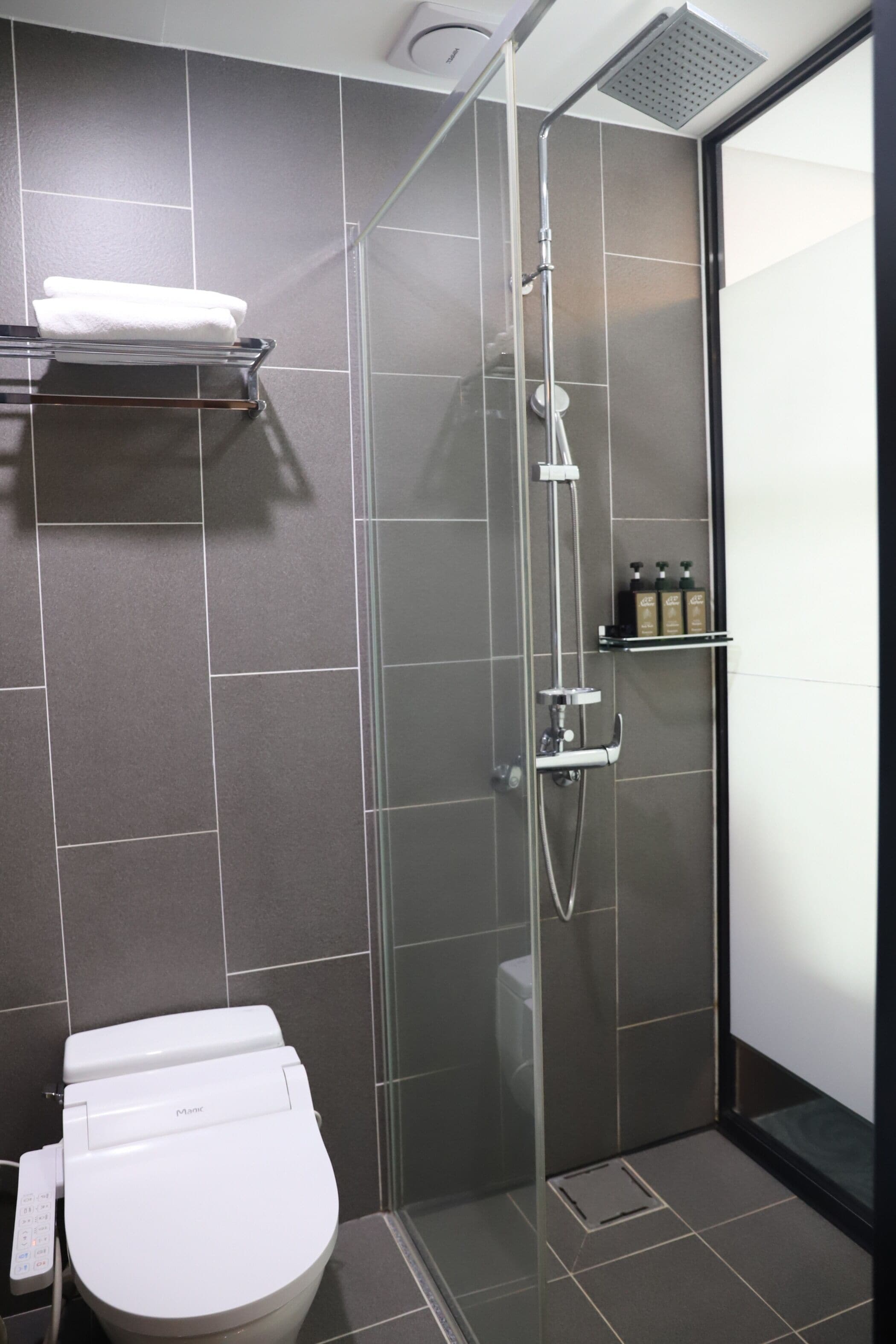 Une salle de bain moderne avec une douche à parois de verre, des toilettes blanches et une étagère contenant des articles de toilette.