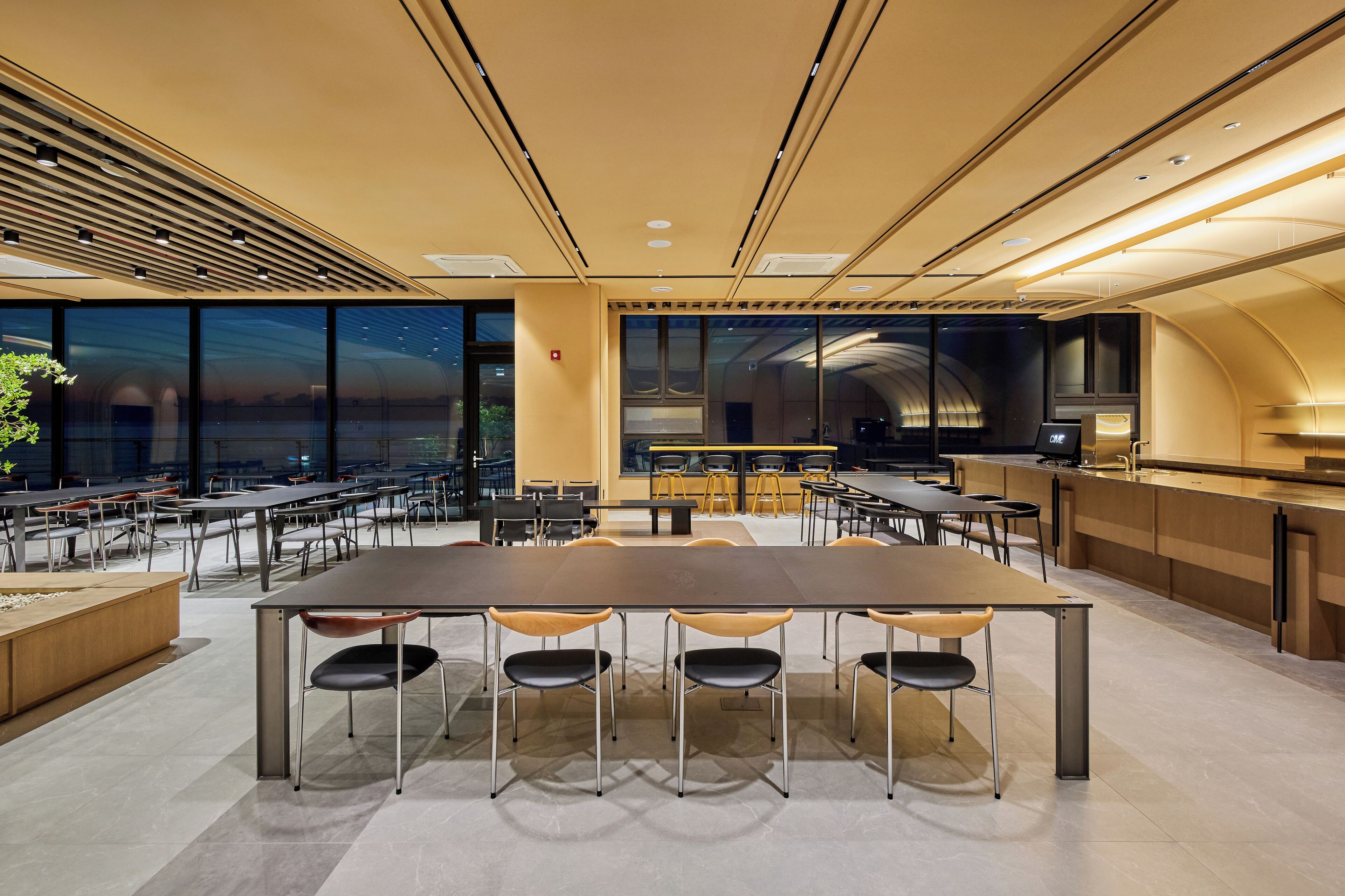 A modern conference room with a large table, multiple chairs, and a kitchen area.