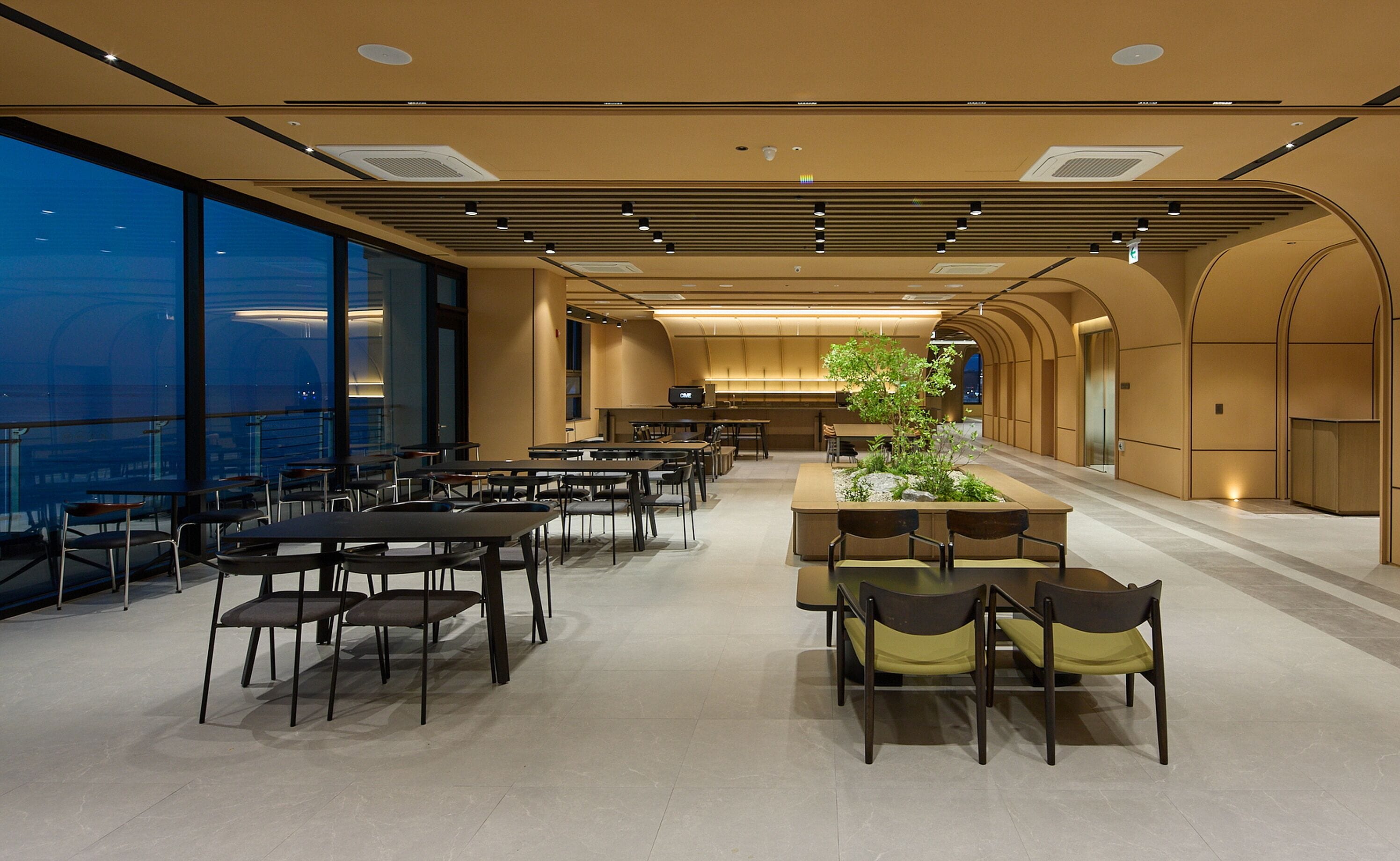 A spacious dining area with high ceilings, large windows, and a central plant feature.