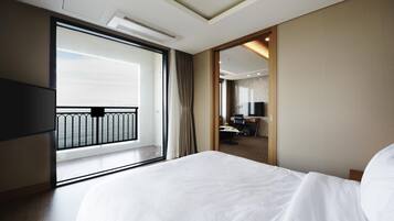 Habitación de hotel con una cama grande, televisión, escritorio con silla y vista al mar desde un balcón.
