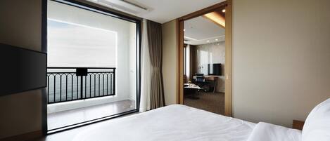 Habitación de hotel con una cama grande, televisión, escritorio con silla y vista al mar desde un balcón.