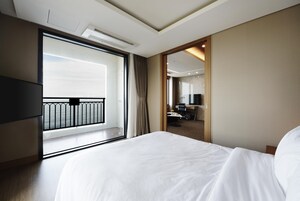 Habitación de hotel con una cama grande, televisión, escritorio con silla y vista al mar desde un balcón.