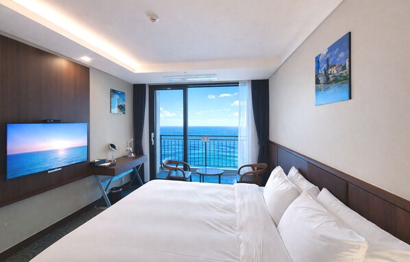 Habitación de hotel con cama, escritorio con televisor, silla y balcón con vistas al mar.