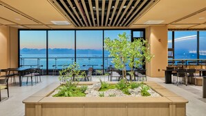 Amplio espacio interior con grandes ventanales con vistas a una masa de agua, que presenta un jardín central con plantas y arreglos de asientos.