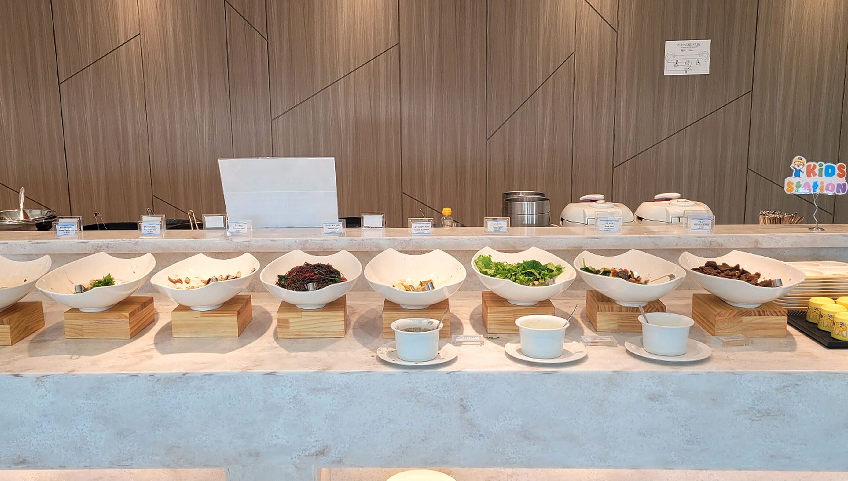 A buffet with various food bowls and utensils on a marble counter.