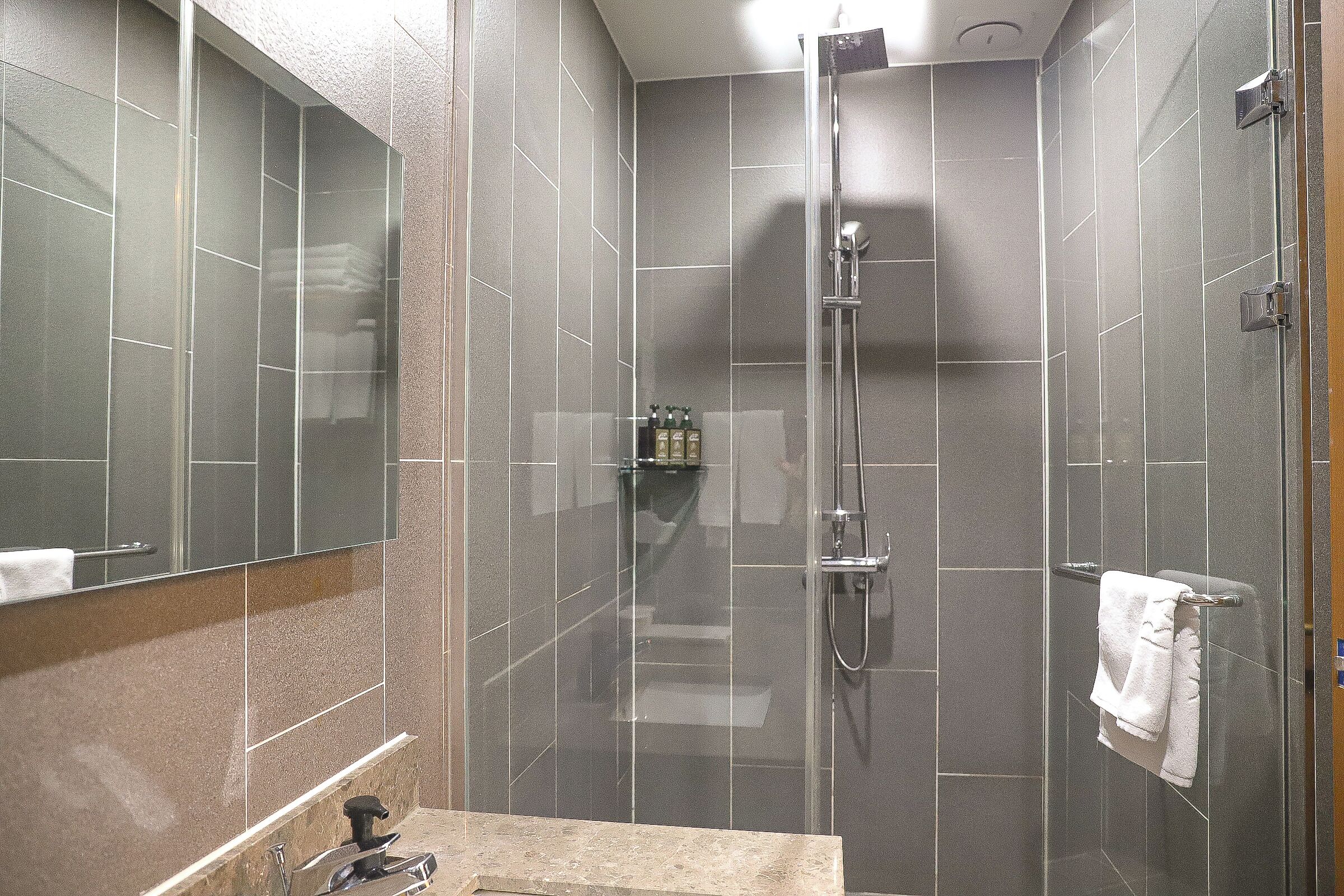 A modern bathroom with a glass-enclosed shower, a large mirror, and a marble countertop.