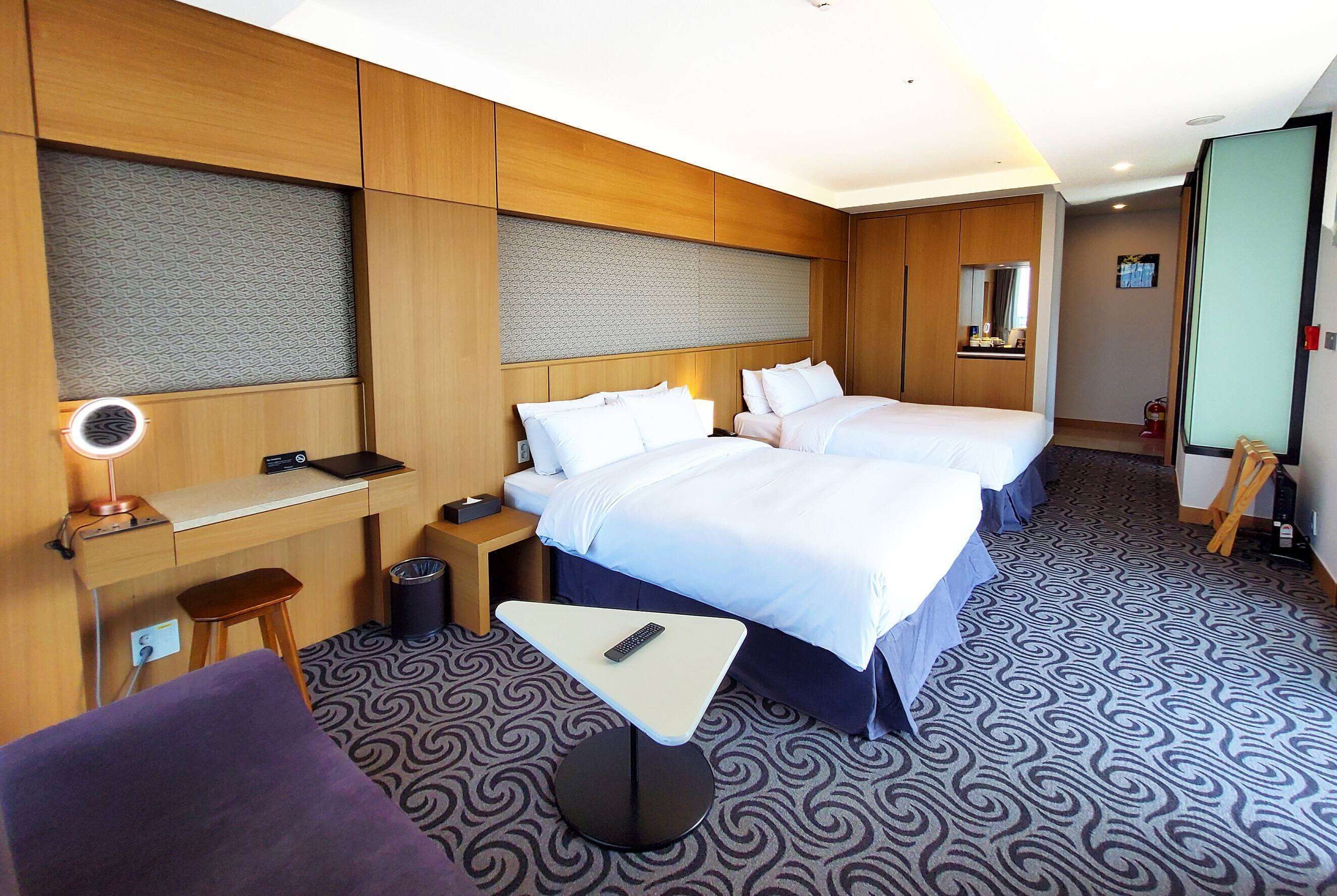 A hotel room with two beds, a desk, a chair, a small table, and a mirror.