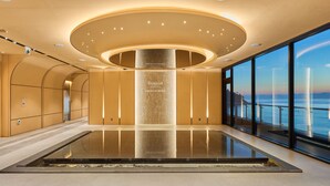 Un interior moderno con una columna central que dice "RAMADA" y "Cafe SEAGARDEN", ventanas amplias con vista al mar y un suelo pulido.