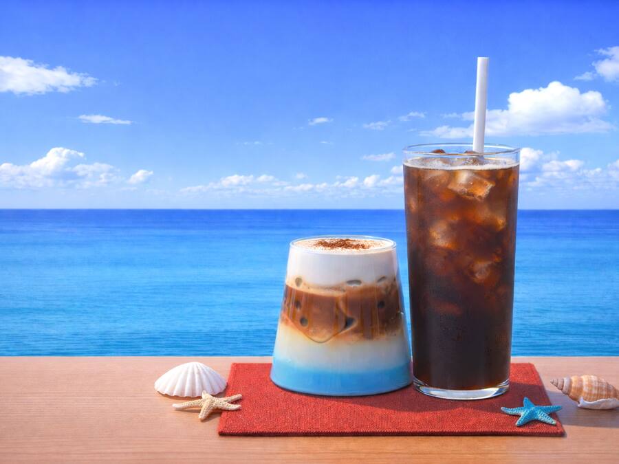 Dos bebidas sobre una mesa de madera con servilleta roja, estrellas de mar y conchas marinas.