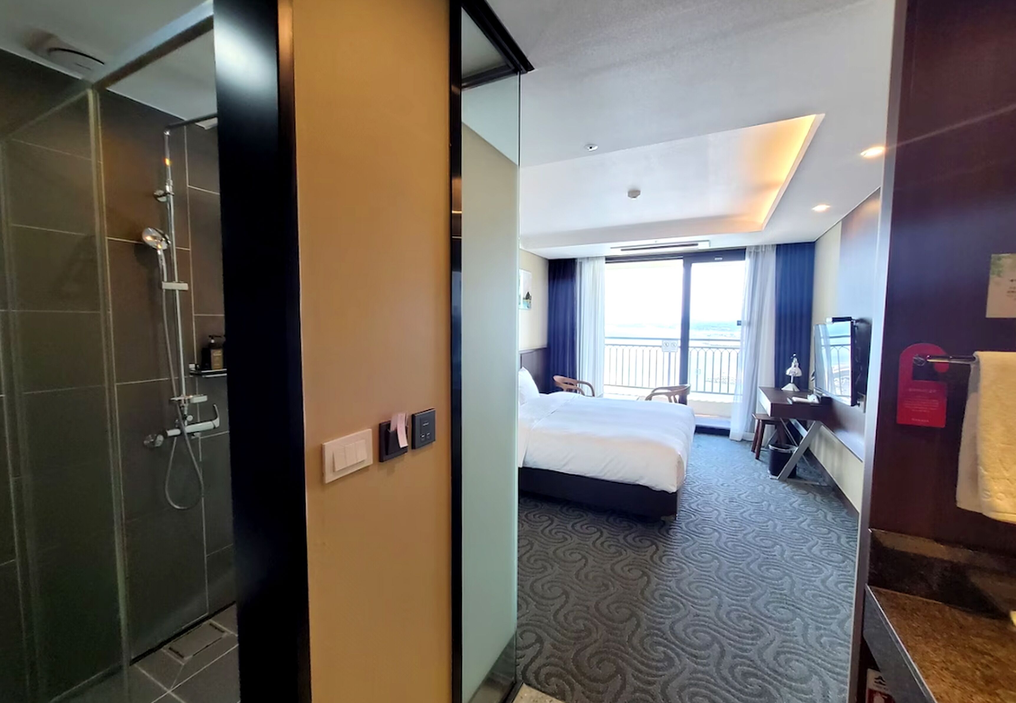 A hotel room with a shower, a bed, a desk, and a view of the outdoors.