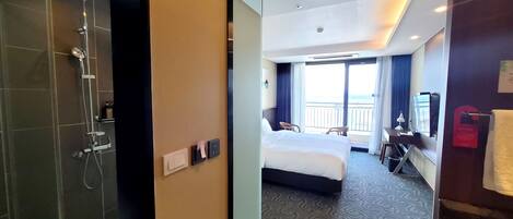 A hotel room with a shower, a bed, a desk, and a view of the outdoors.