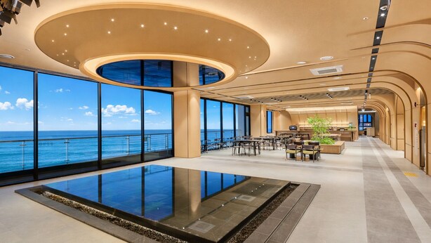 Amplio espacio interior con grandes ventanales que ofrecen vistas al océano, una piscina central y una zona de estar con mesas y sillas.
