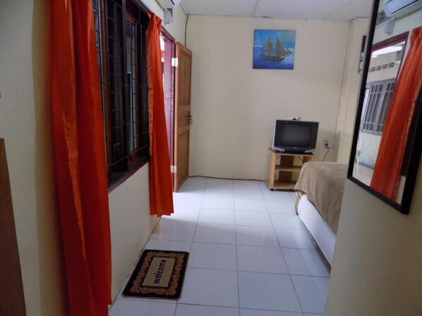 Una habitación pequeña y acogedora con una cama, un televisor sobre un pedestal de madera, un felpudo y un cuadro en la pared.