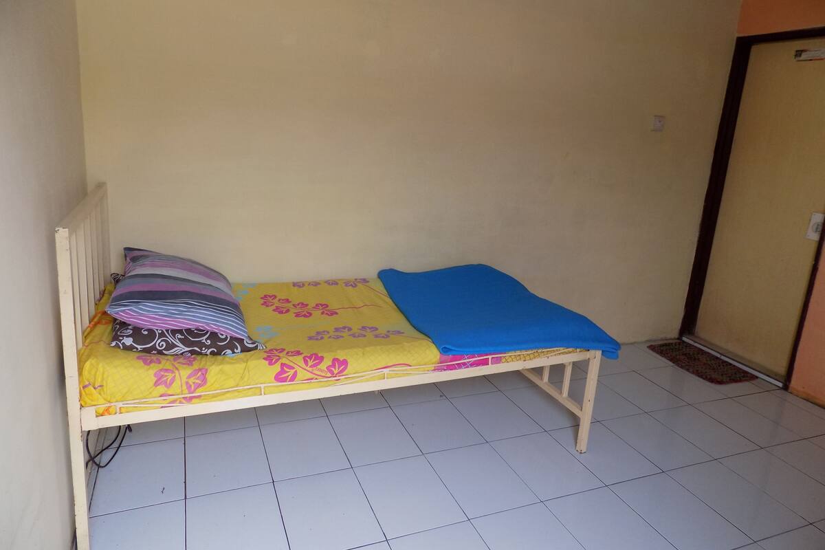Una habitación pequeña con cama individual, pared lisa y suelo de baldosas.