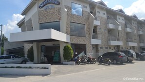 Voici un hôtel avec une enseigne indiquant « Boomerang Hotel ». Il présente un design moderne, avec un toit plat et un balcon au deuxième étage. Plusieurs voitures sont garées devant, et une moto se trouve à l’intérieur.