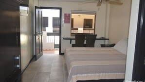 Une chambre d’hôtel équipée d’un lit, d’un bureau, d’une chaise, d’un ventilateur de plafond et offrant une vue sur la cuisine et l’espace repas.
