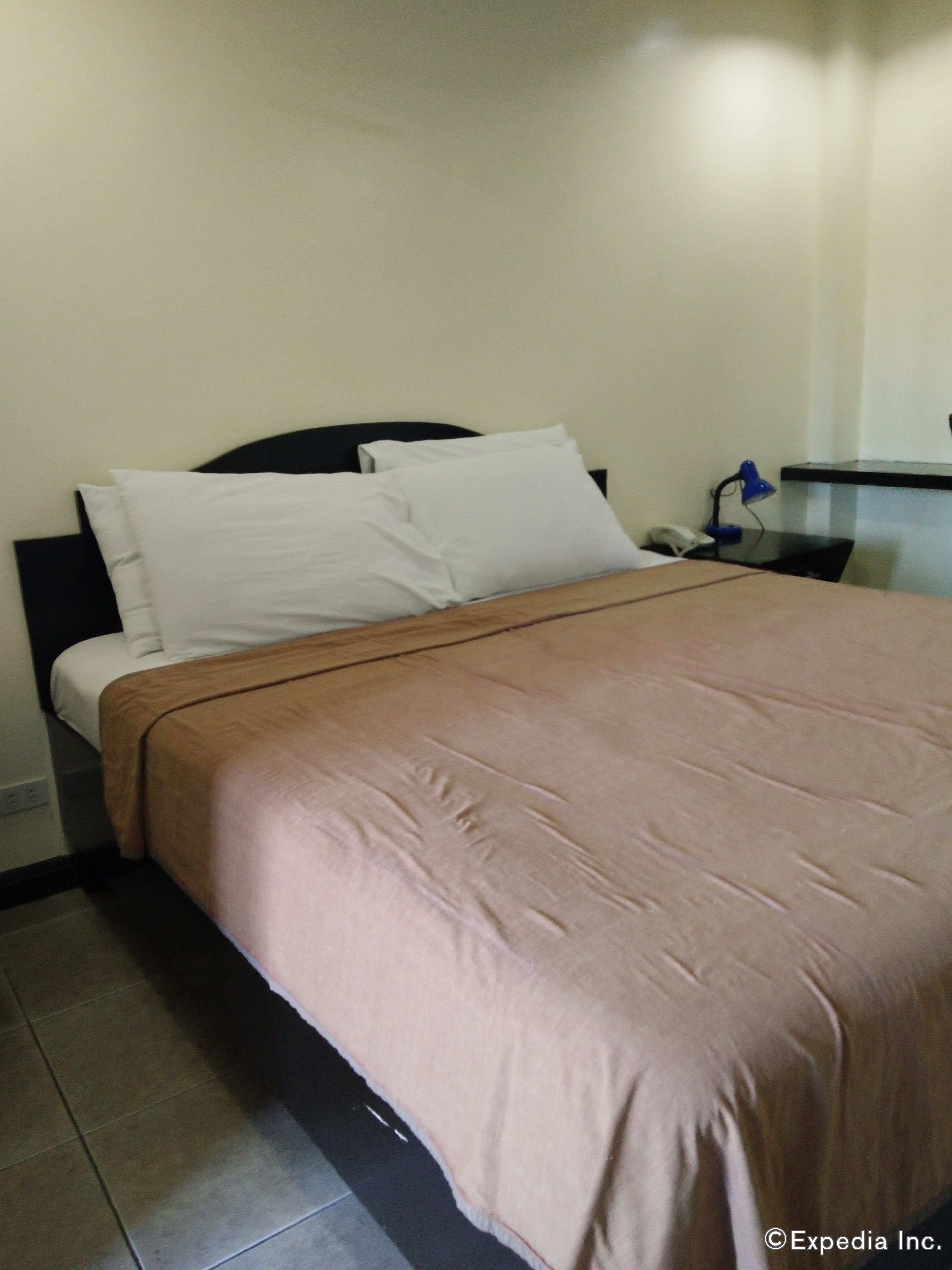 Una cama bien hecha con almohadas blancas y una colcha marrón en una habitación de hotel.