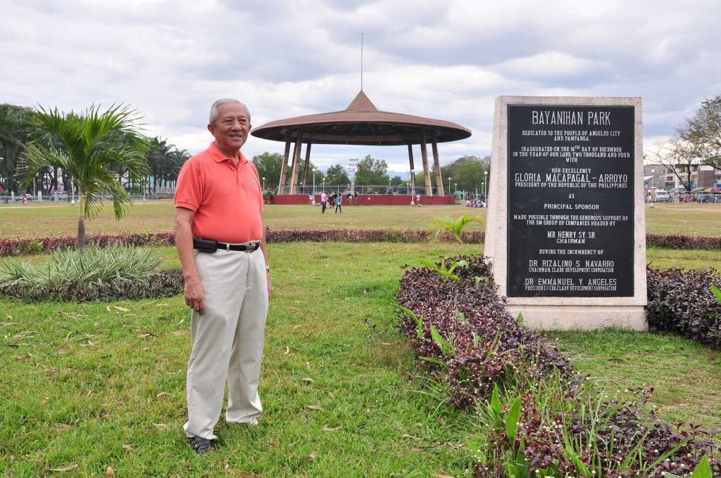 A man standing in a park with a gazebo and a signboard.