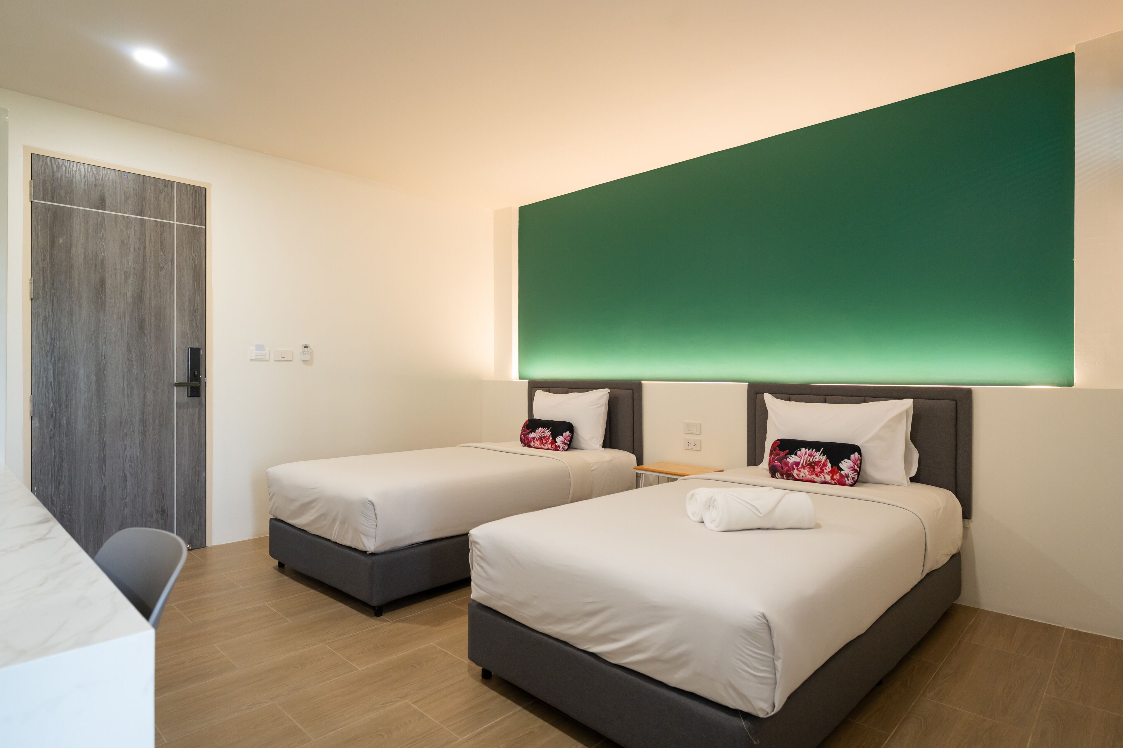 Habitación de hotel con dos camas, un escritorio y una pared de detalles en color verde.