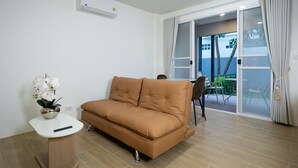 A modern living room with a brown sofa, a small white table with a remote control, and a potted orchid. - KYP Hotel (Fang)